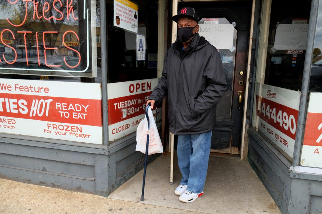 Roosevelt Washington stands with his lunch to-go in a bag on Burleigh Street. Growing up in the community, he ate here with his parents a generation ago. No longer a resident, he revisits to get a pasty or two and says he likes them with hot peppers and cheese.