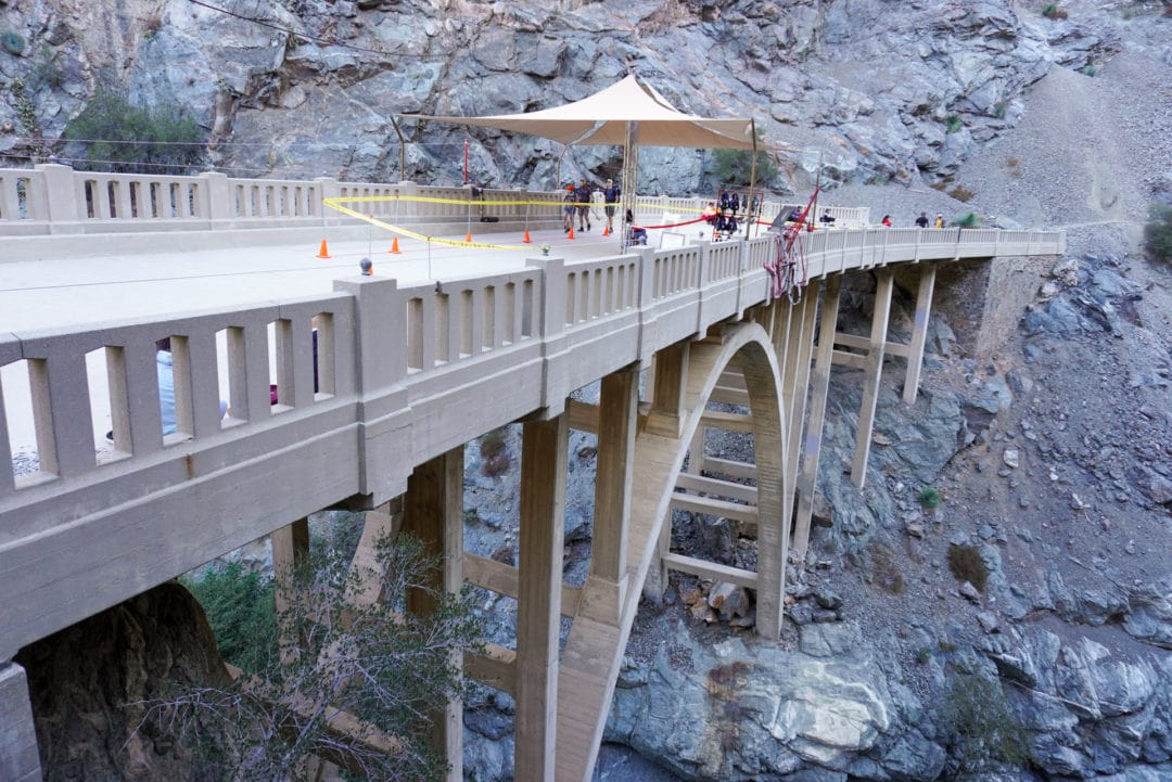 A handful of people walking on an arch bridge set above a deep canyon.