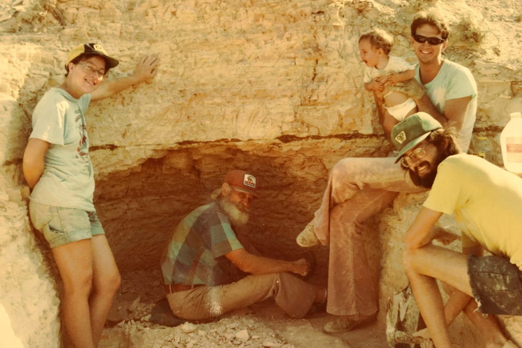 four men and a baby hunt for fossils in a rock formation
