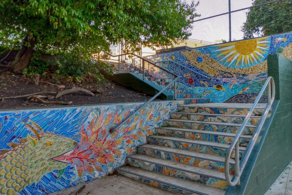 Mosaic stairs starting with tip of a dragon’s tail and ending with two mosaic murals of a fire-breathing, scaly dragon and the solar system at the top