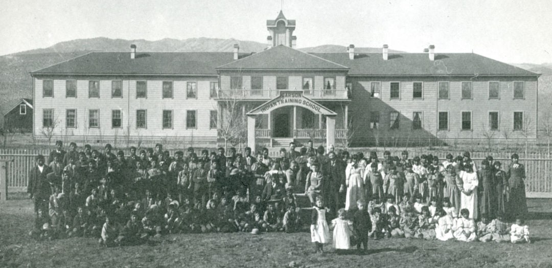 Students pose for a group photo in front of one the original wooden buildings