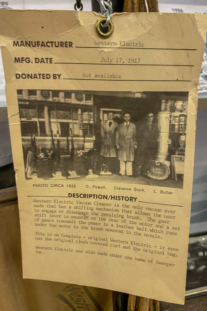 A yellowed and typed card detailing the history of a vintage vacuum with a black and white photo of Clarence Stark