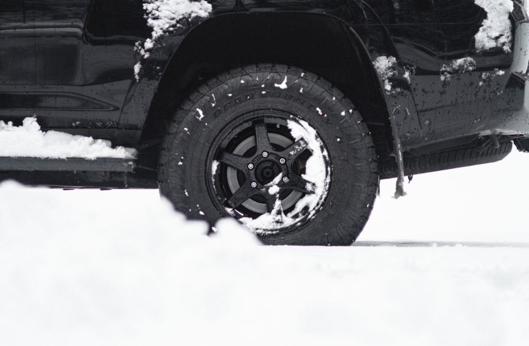 Close up of black tire with black rims with some snow on the tire and around the car frame