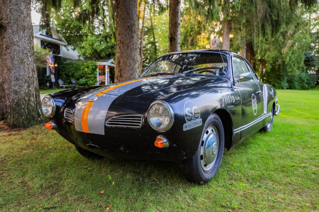 A black vintage sports car with gray and orange racing stripes is parked on a lawn.