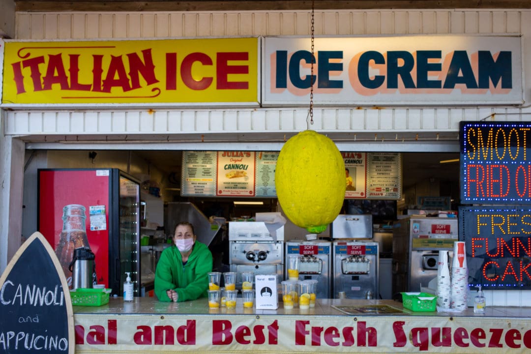 a snack shop with an employee wearing a facemask and signage that says "italian ice" and "ice cream"