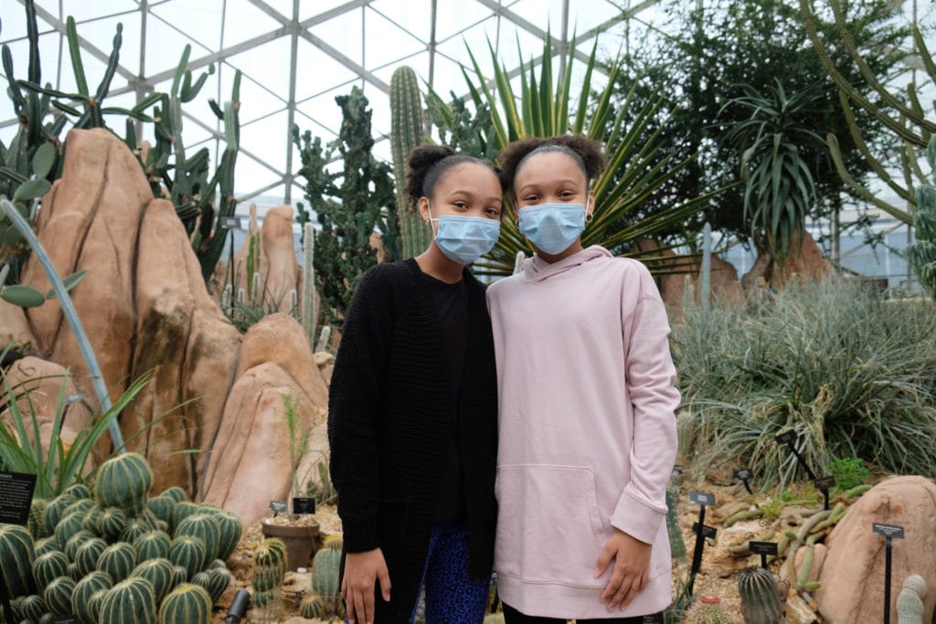 twin girls wearing face masks pose in front of a desert backdrop