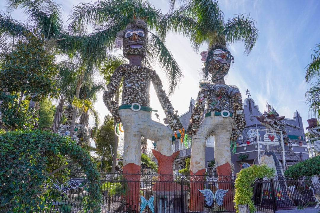 Two tall, human-like sculptures made from palm trees, surrounded by other art pieces.