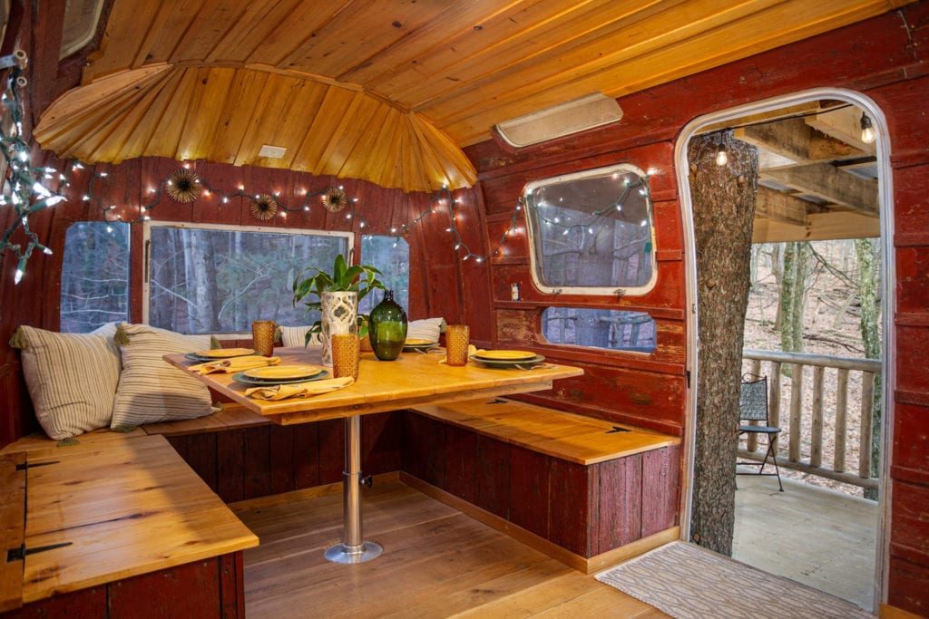The interior of an Airstream with wood paneling, string lights and a dining nook