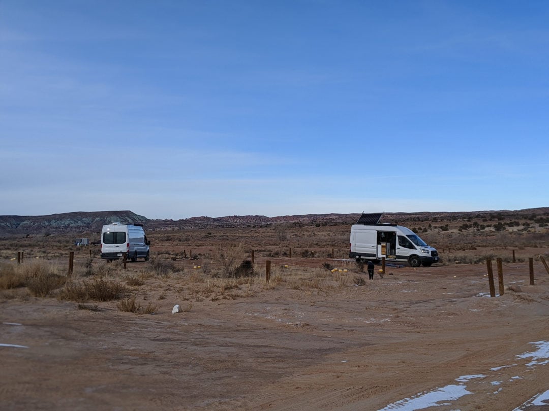 Two white vans parked in the desert against a clear blue sky