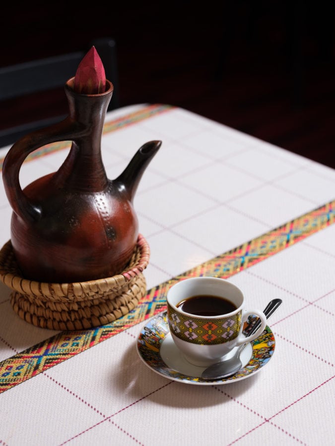 Close up of small cup of coffee with special Ethiopian coffee pot in woven basket on white table cloth