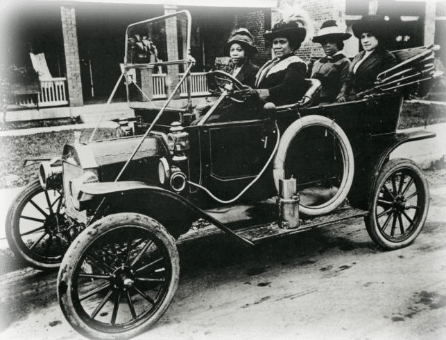 Black and white photo of four Black women driving an early 1900s automobile 