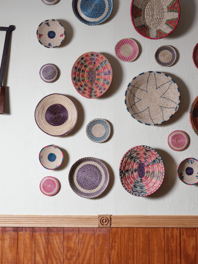 Various colored woven plates and baskets hanging on white wall