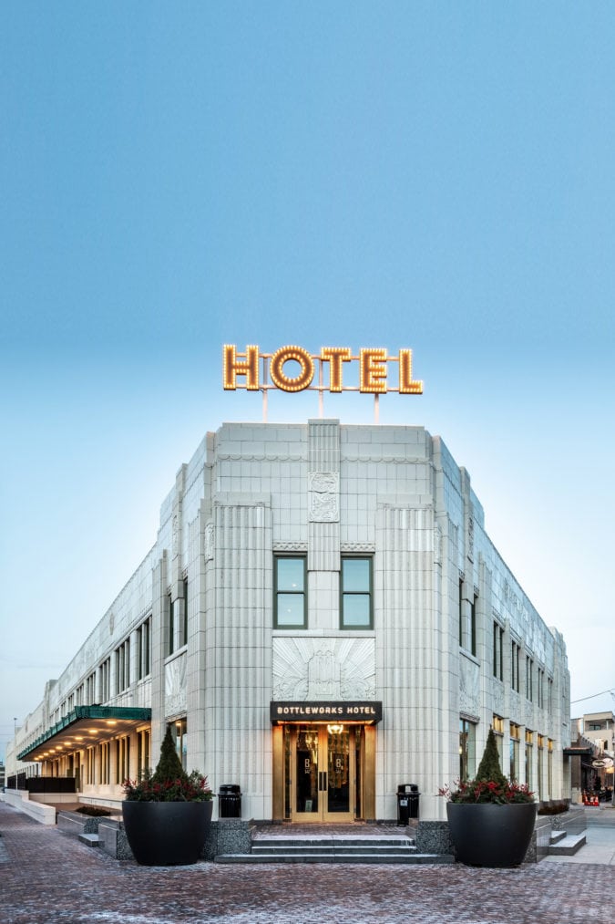 a white art deco building against a blue sky with a bulb sign lit up spelling out hotel
