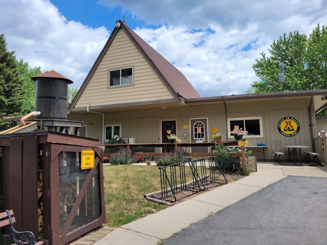 Brown, A-frame building with empty bike rack and firewood for sale out front on a grassy lawn