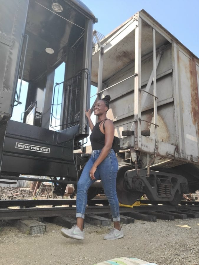 Woman in jeans walks in front of a stationary train on the tracks