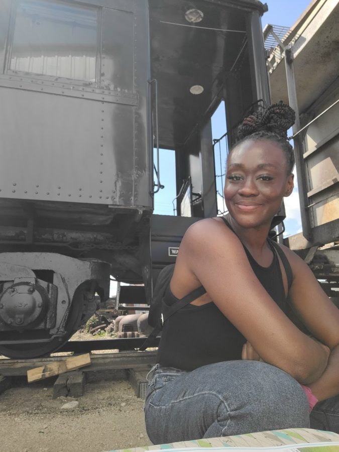 Woman in jeans poses in front of stationary train on the tracks with a slight smile