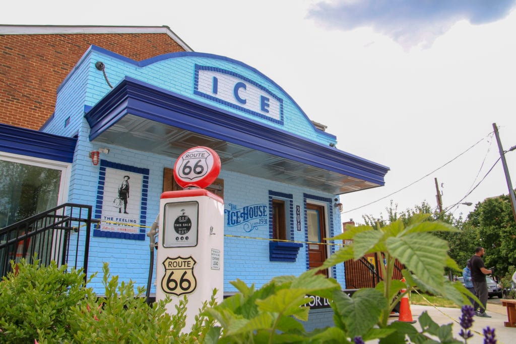 a blue brick building with the word "ice" painted on top and a vintage gas pump outside