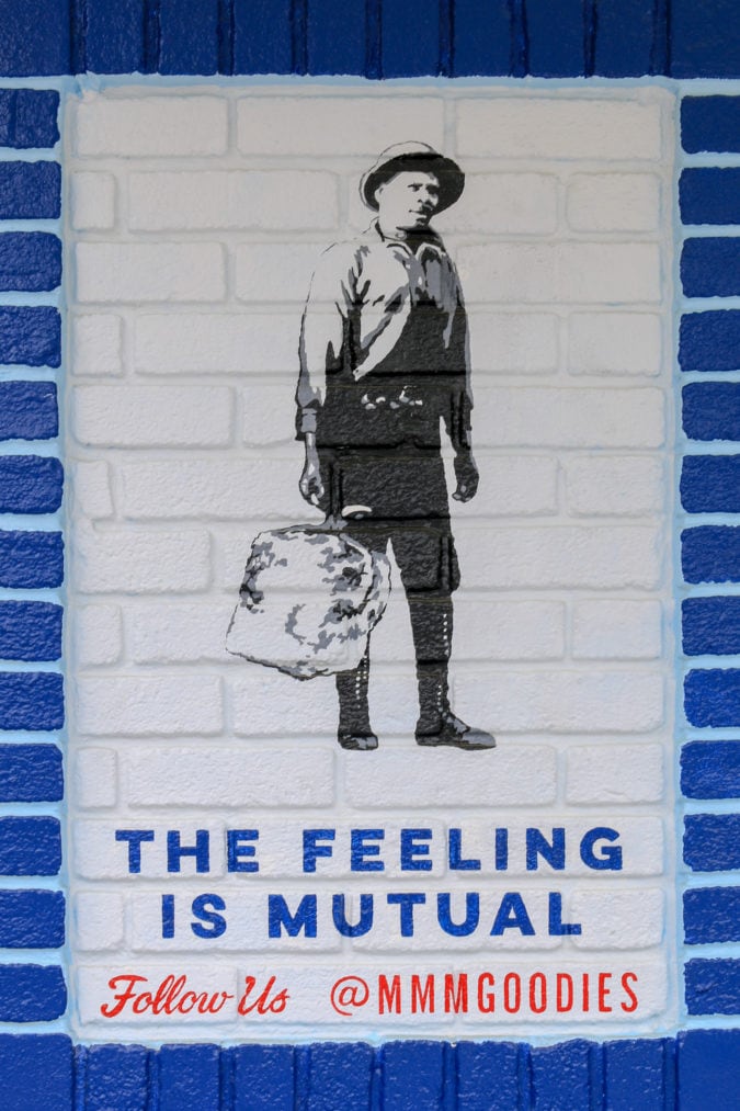 a sign painted on the side of brick building featuring a black man carrying a bag of ice and the words "the feeling is mutual"