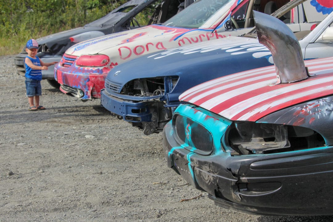 a line of cars painted red white a blue with a small white child in a tank top and flip flops standing nearby
