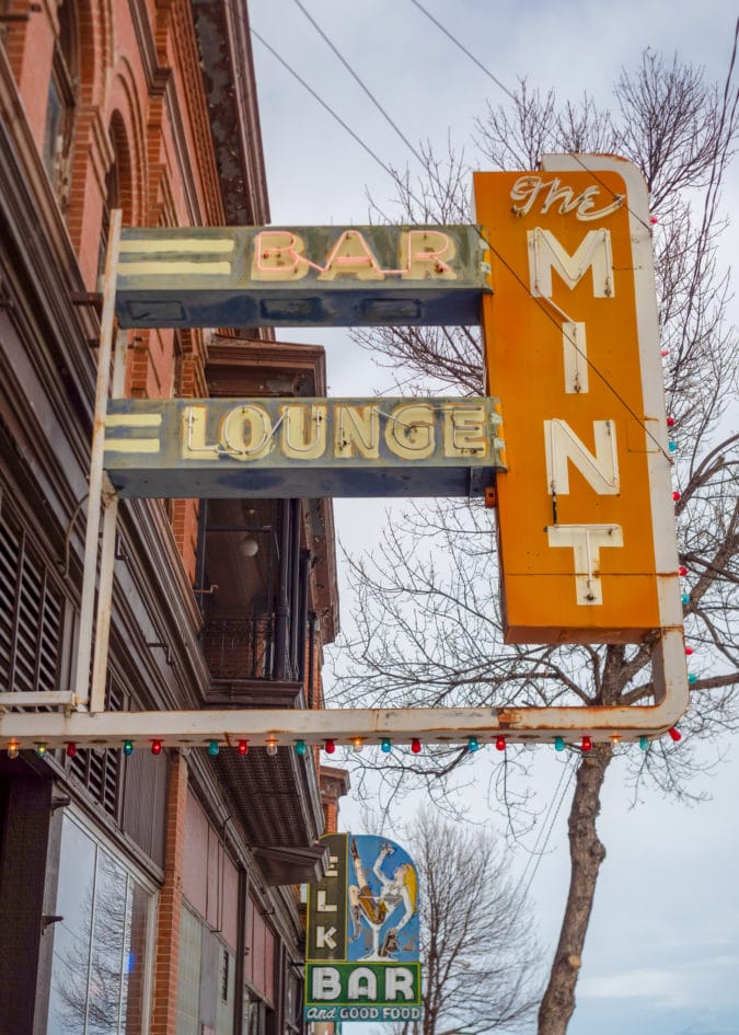 a neon sign that says "bar and lounge the mint" in green and orange wrapped in christmas lights