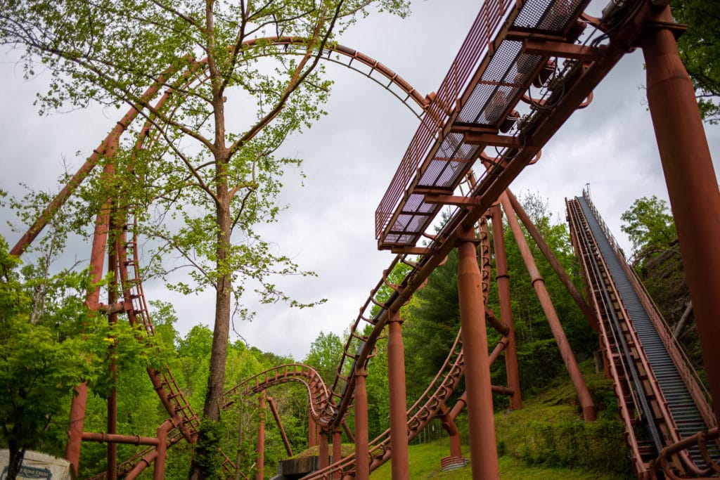 an orange steel rollercoaster track set against a lush green backdrop