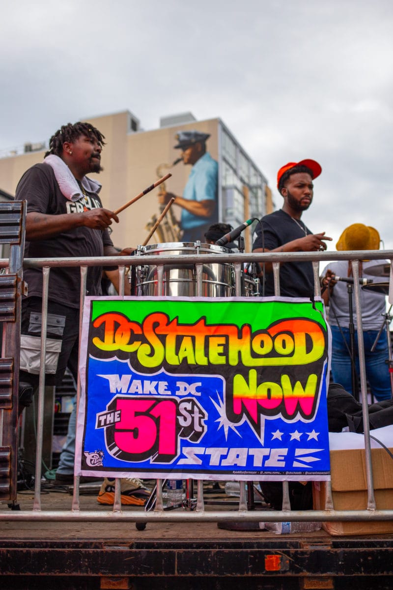 A colorful poster that says "DC Statehood NOW" hangs on a truck that hosts a band