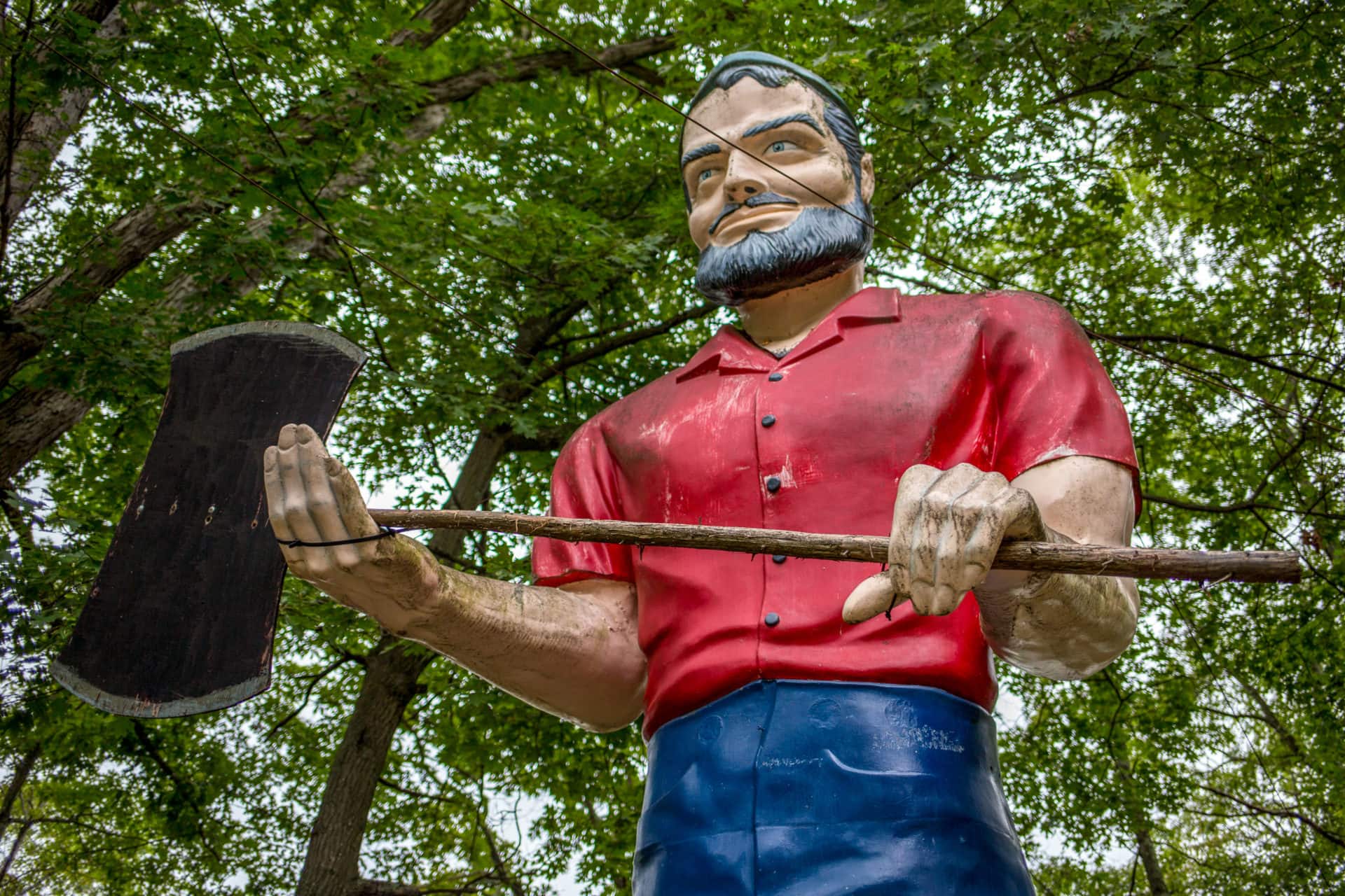 a fiberglass muffler man with a red shirt and grey beard clutching an axe