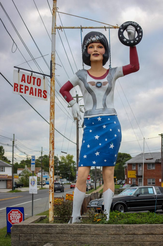 a female fiberglass statue holds a tire and is dressed like wonder woman