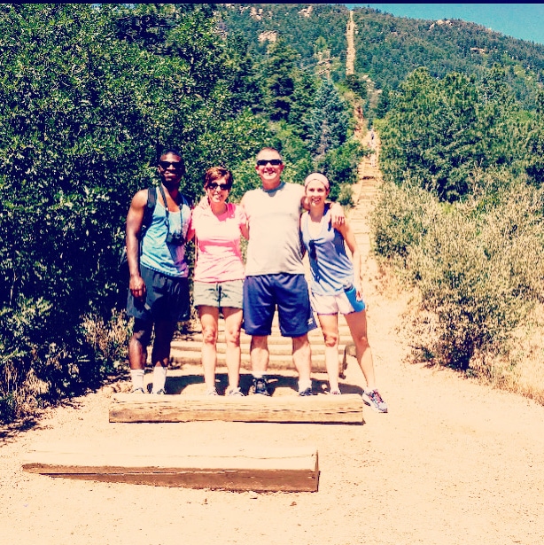 a black man, two white women and a white man stand smiling on a hiking trail outside