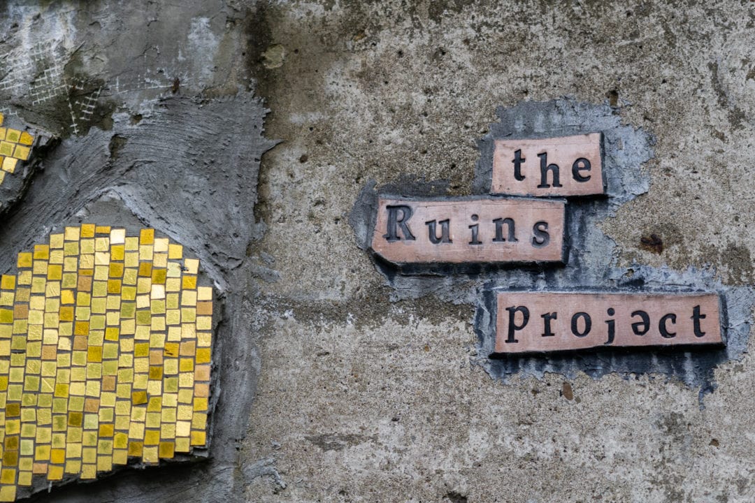 a yellow mosaic next to a sign that reads "the ruins project"