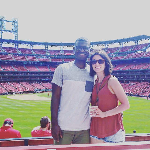 a black man and white woman stand smiling in a baseball stadium