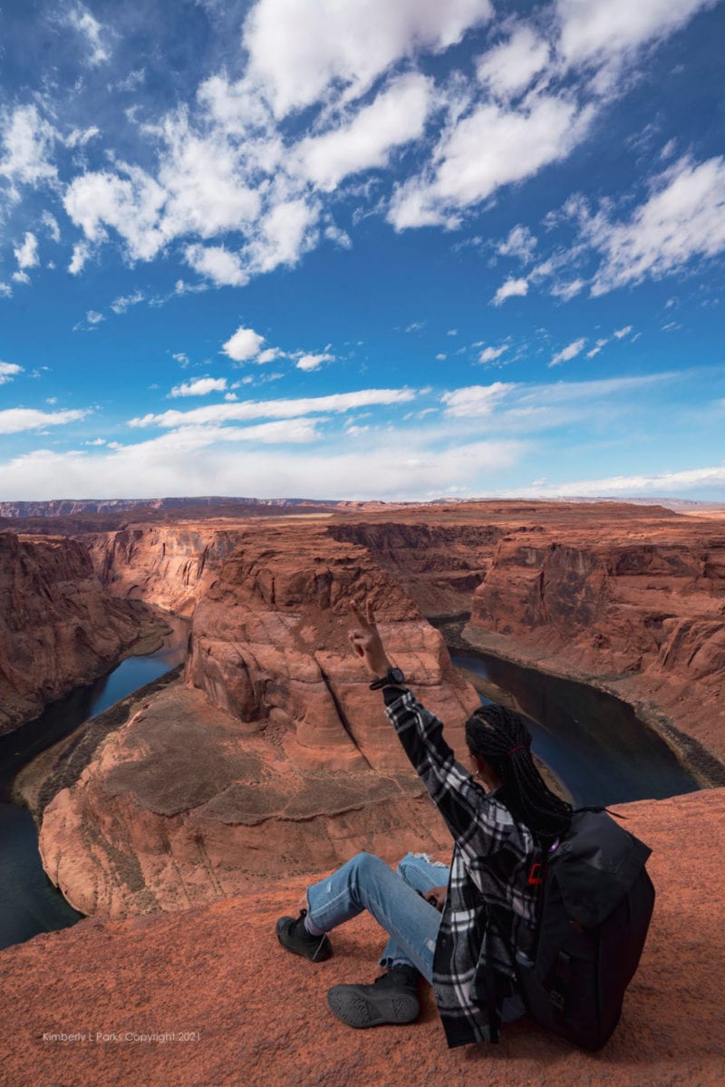 A woman raises two fingers in the air while overlooking Horseshoe Bend