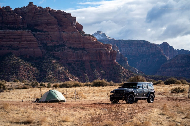 A Jeep parked in the desert next to a tent, surrounded by red rocks