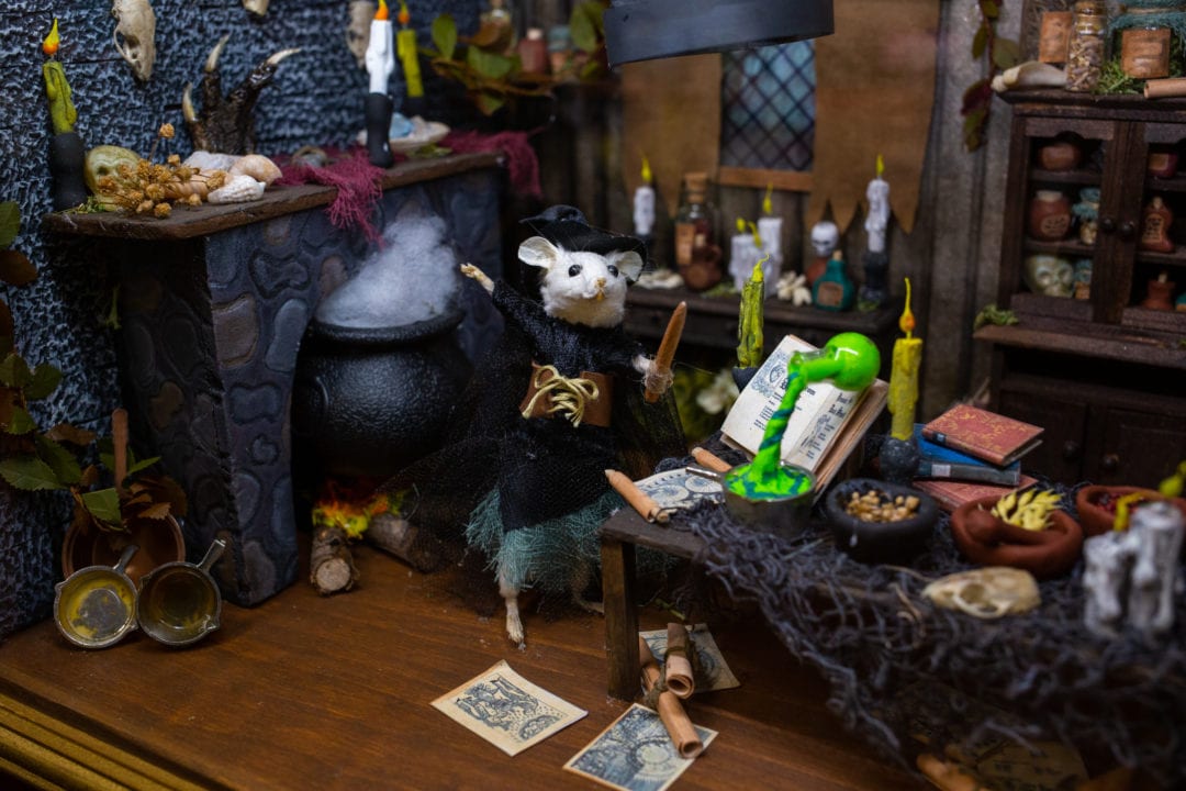 A taxidermy mouse is dressed as a witch surrounded by a spooky scene