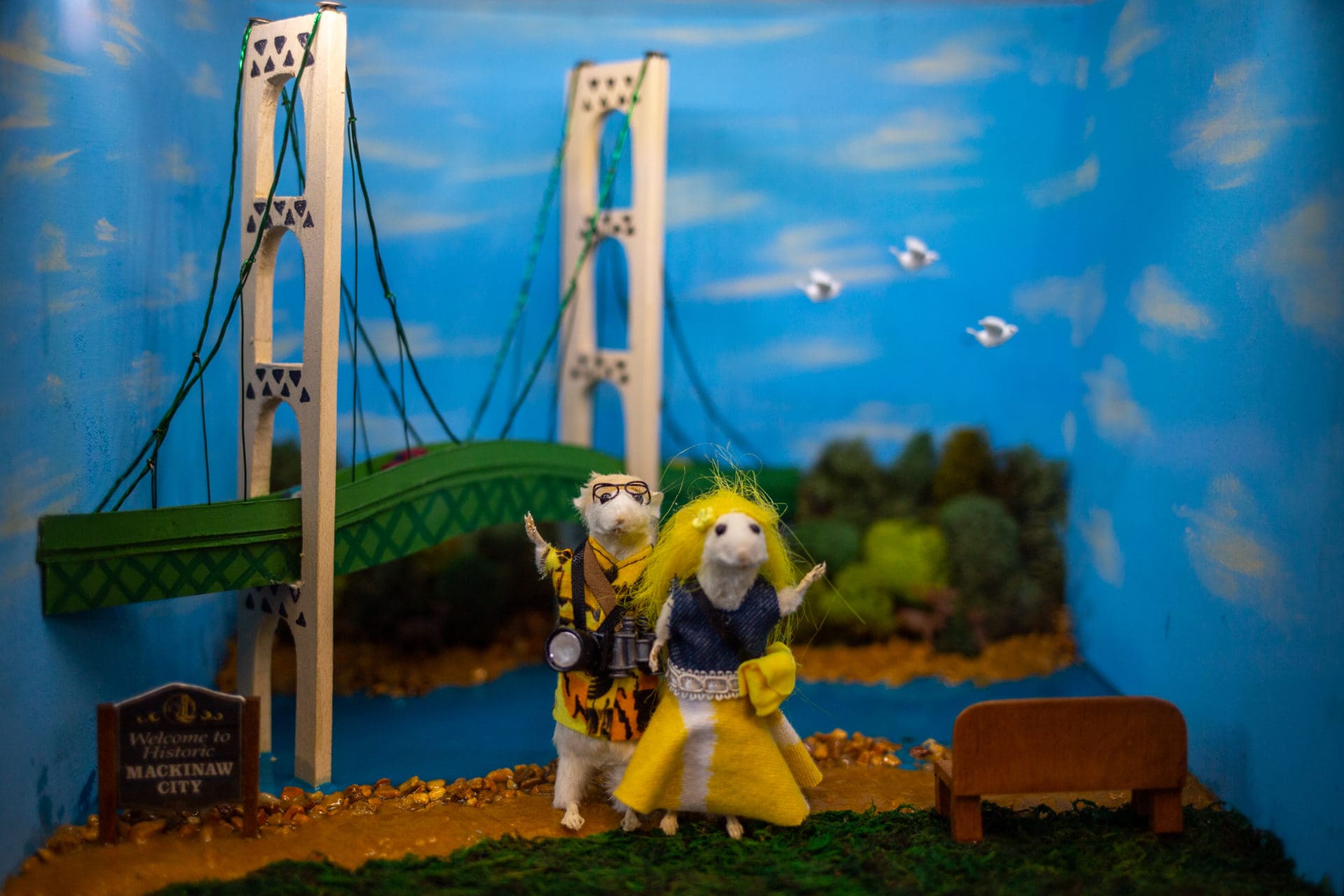 Two taxidermy mice posed and dressed as tourists in front of a miniature Mackinac Bridge