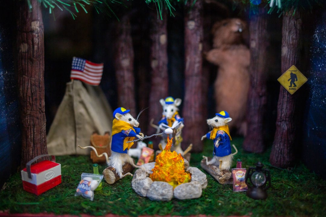 Taxidermy mice dressed as boy scouts roast marshmallows over a campfire in the woods