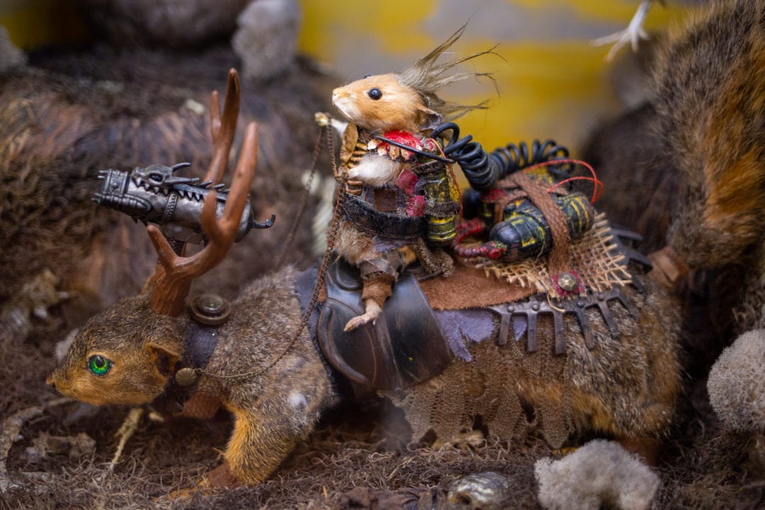 A taxidermy mouse in steampunk gear rides a taxidermy squirrel with horns