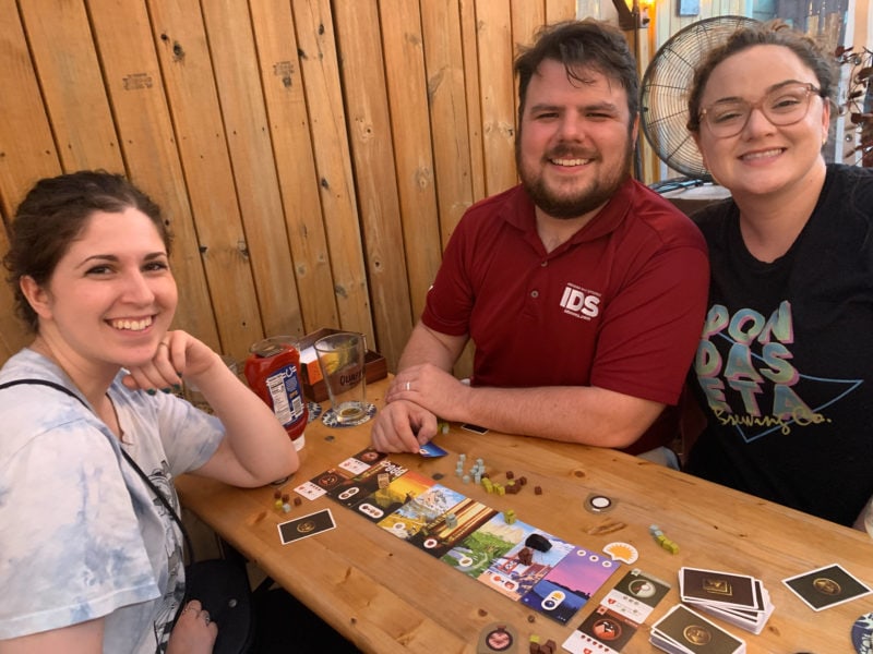 Three people playing a board game and smiling at the camera
