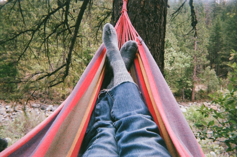 POV of two socked feet in a hammock surrounded by forest 