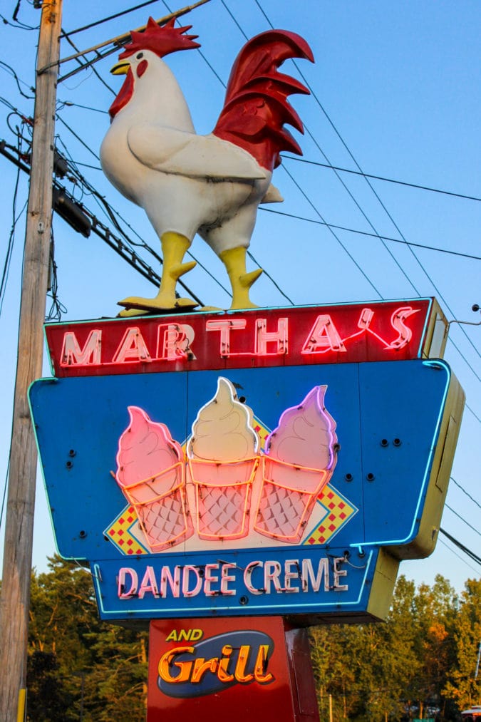 a neon sign topped with a rooster that says "martha's dandee creme"