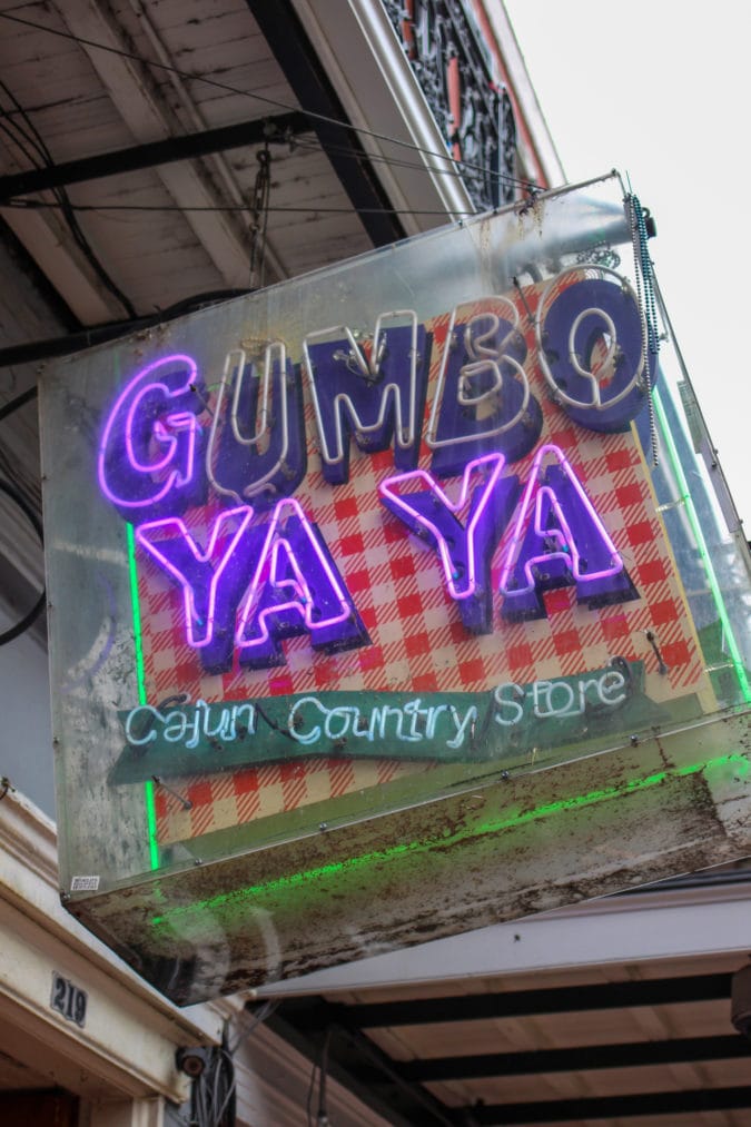 A partly-lit neon sign featuring the words "Gumbo ya ya"
