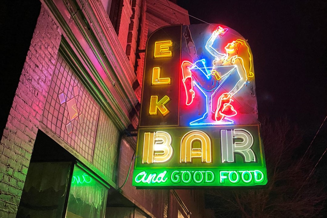 the elk bar sign at night featuring a woman in a martini glass and the words "elk bar and good food"