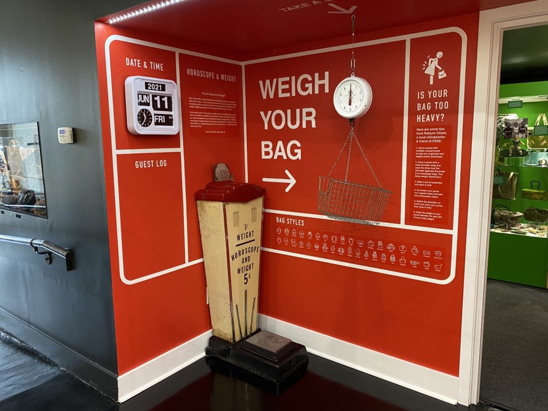 a museum display with a red wall and a scale with type that says "weigh your bag"