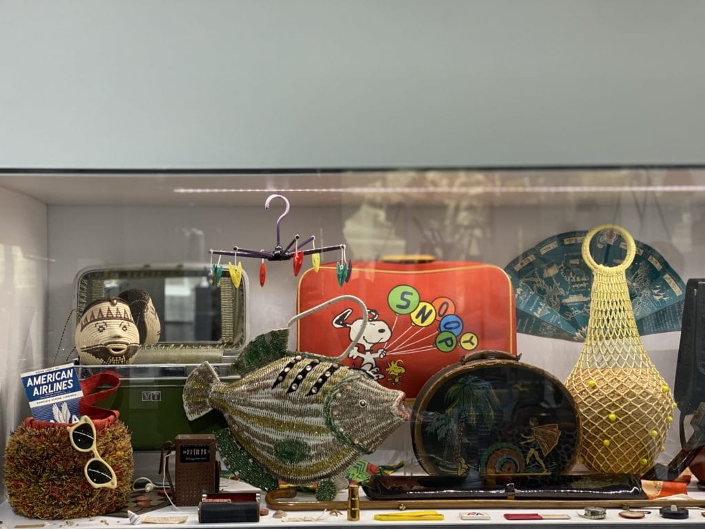 a display of purses including a red one with snoopy and a straw purse shaped like a fish