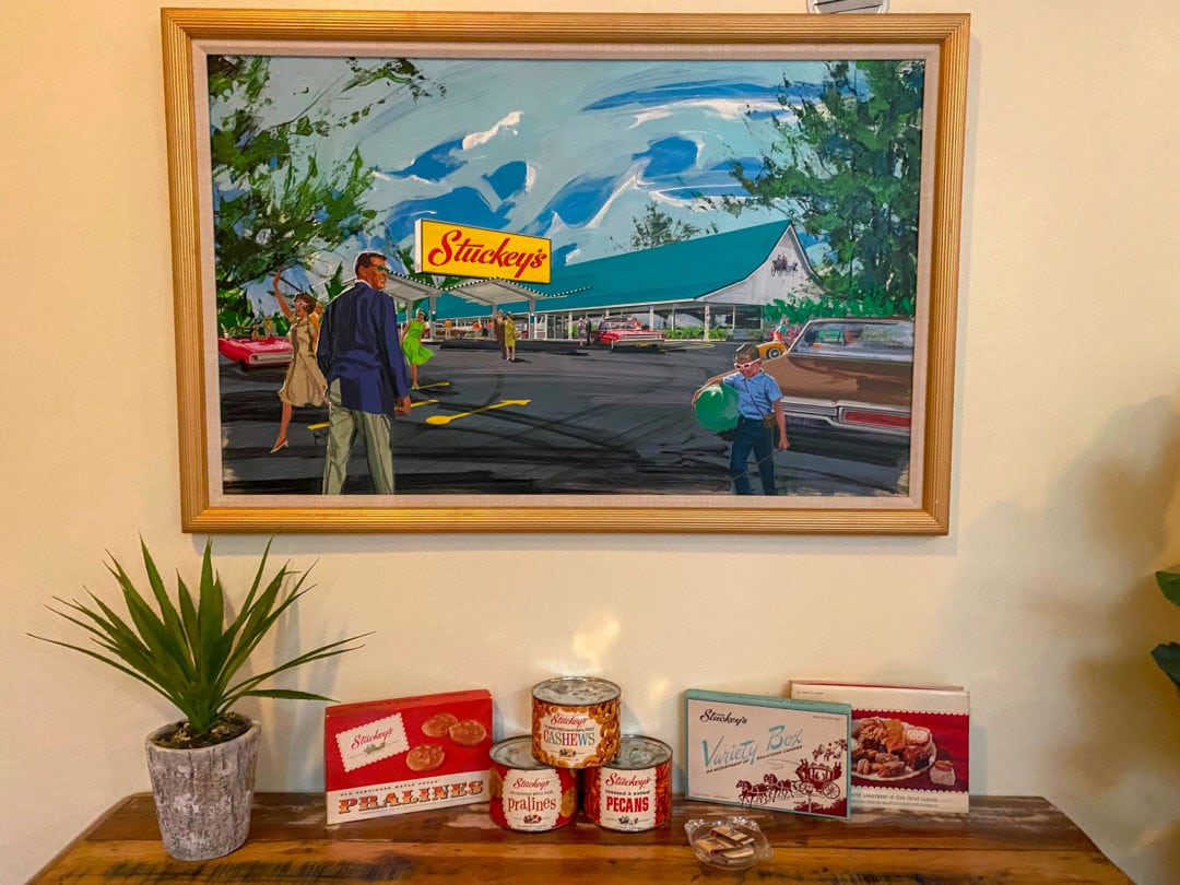 A painting of Stuckey's hangs above a table with a plant, cans of pecans, and boxes of candy