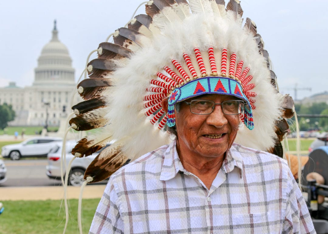 A man in a traditional feather and bead headdress in front of the Capitol.