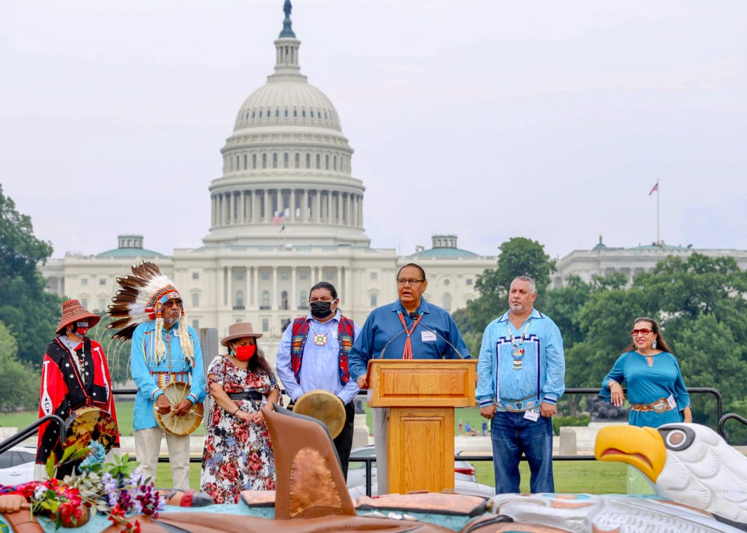 Native organizers stand behind a podium and address the crowd in front of the capitol