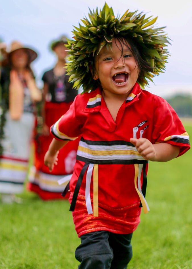 a kid wearing a greenery headdress runs and smiles at the camera