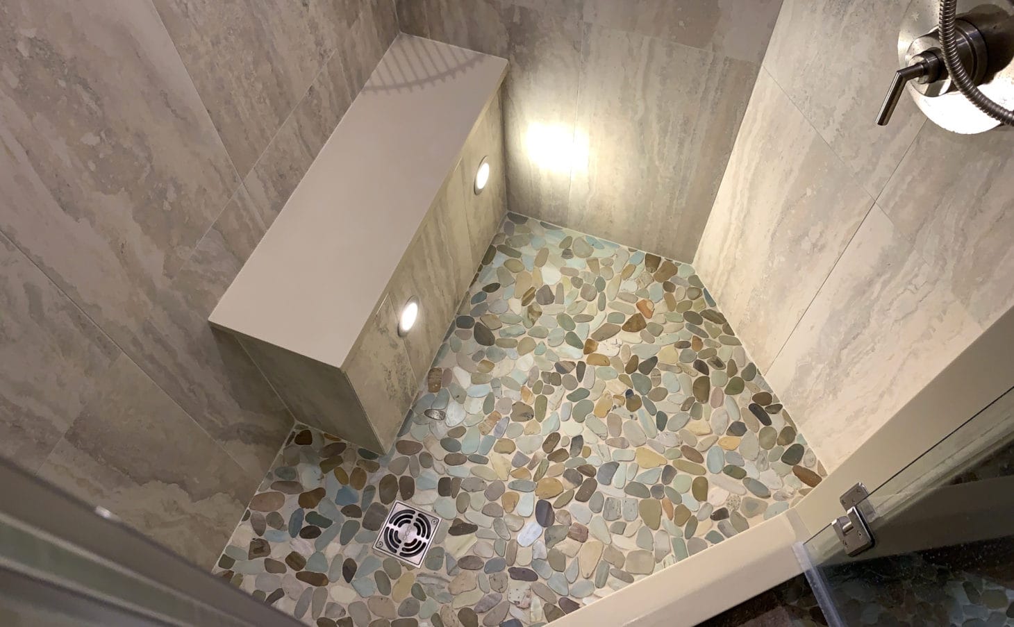 Pebble stone shower floor with lighting and bump out seat in a luxury RV shower