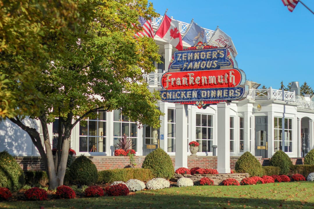 a red and blue neon sign that says "zehnder's famous frankenmuth chicken dinners" outside of a white building